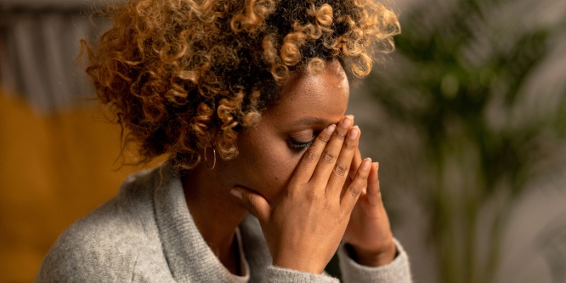 a picture of a black woman with blondish curly highlights holding her face and struggling with anxiety
