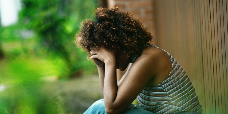 Person sitting outdoors with their head resting in their hands